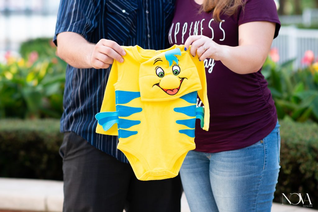 Soon to be parents holding a newborn flounder outfit during their maternity photo session.