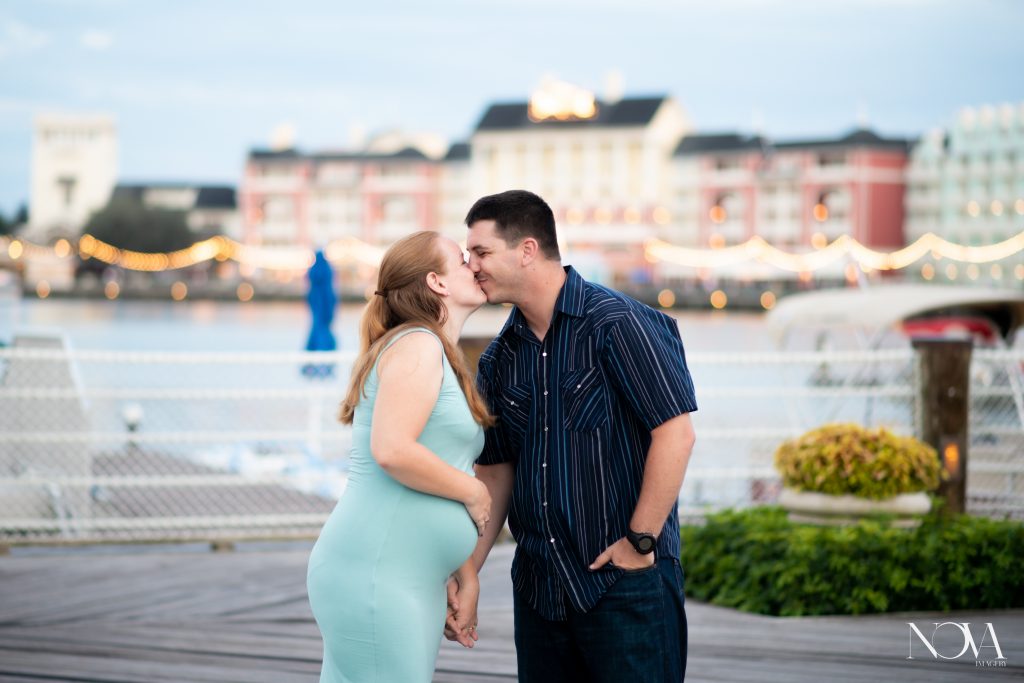 Soon to be parents kissing during maternity photoshoot, with Disney’s Boardwalk in the background.