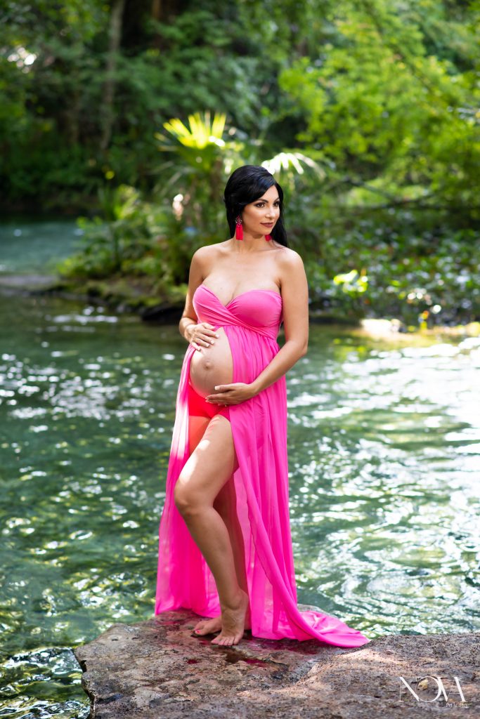 Pregnant mom cradling belly in a pink maternity gown during Kelly Park photo session.