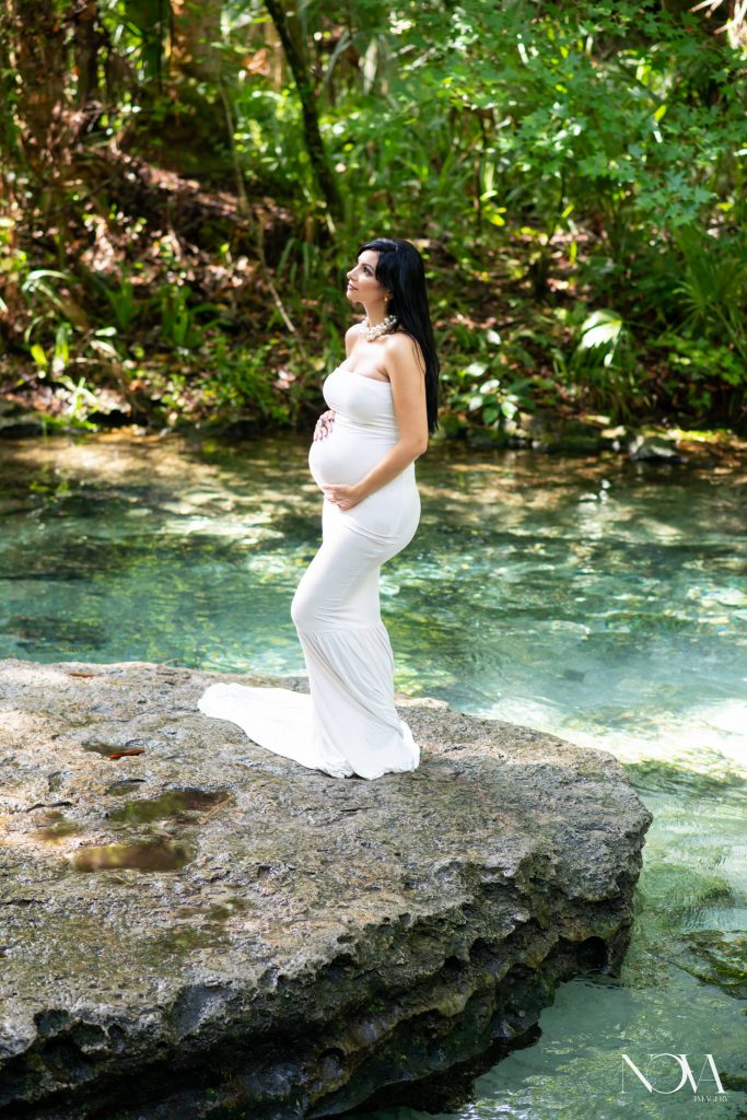 Pregnant mom holding belly, in a white maternity dress, at Kelly Park.