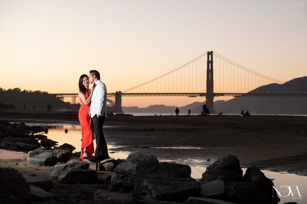 Groom kissing bride-to-be’s forehead in front of Golden Gate Bridge during their San Francisco engagement session.