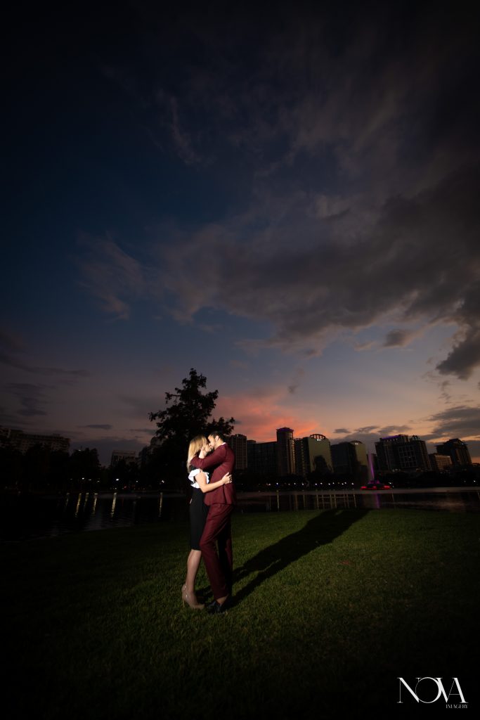 Couple kissing with Orlando city skyline in the background for their Lake Eola engagement session.